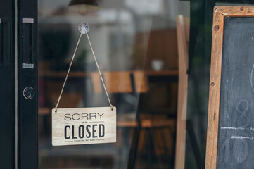 Sorry we're closed sign board hanging on a dirty glass door.