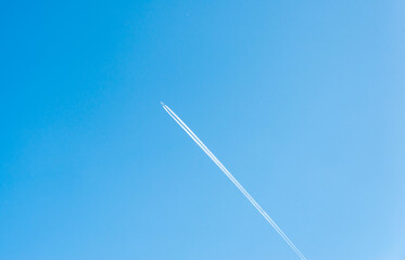 The plane flies up in the blue sky leaving traces behind it 
