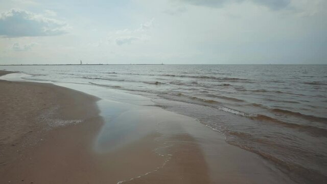 Summer on the yellow sandy Baltic beach in Latvia. Sunny day at the mouth of the Daugava river in the Gulf of Riga. Ships are in the roadstead to enter the port. Waves rhythmically roll over the