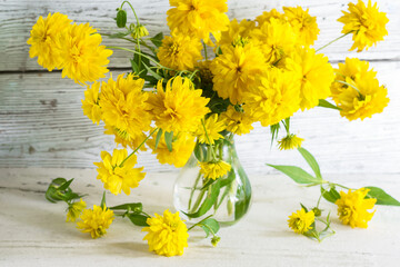 Bouquet of yellow color vivid dahlia flowers in a vase in bright wooden background, still life with...