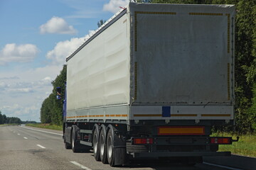 Beautiful van semi truck driving on the suburban highway road at Sunny summer day on blue sky with white clouds background, cargo trucking transportation logistics, back side close-up view