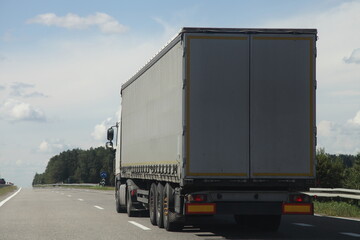 One European awning van semi truck back side close-up view drive on the suburban highway road at Sunny summer day on blue sky with white clouds background, cargo trucking transportation logistics