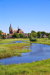 Fototapeta na wymiar View over green wetland water on cityscape of durch town with tower of medieval church against blue summer sky - Neer (Limburg), Netherlands
