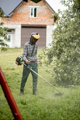 Worker with a gas mower in his hands, mowing grass in front of the house. Trimmer in the hands of a man. Gardener cutting the grass. Lifestyle.
