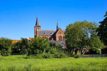 View over lush green pasture and trees on small dutch idyllic village with medieval old church against blue cloudless summer sky - Neer (Limburg), Netherlands