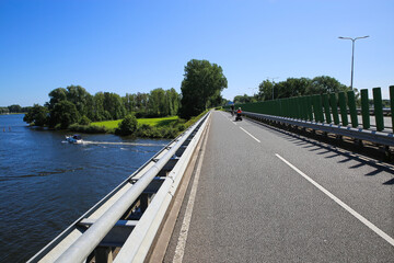 View on cycling track on bridge along beautiful lake (noorderplas) with green landscape against blue summer sky - Roermond, Netherlands - obrazy, fototapety, plakaty