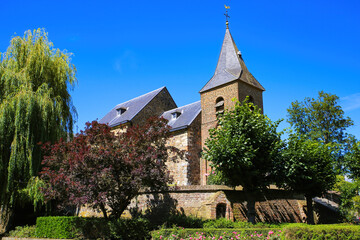 View on medieval church and fortress in rural dutch landscape with green trees against blu summer sky - Sint Dionysiuskerk in Asselt near Roermond, Netherlands