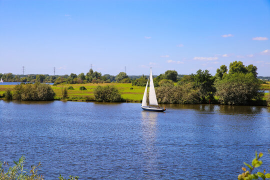 View on sailboat on river maas (asselste plassen, Asselt) in rural green landscape against blue summer sky - Netherlands, Roermond