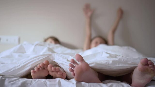 Pair of feet in bed on white sheets. Child lies in bed in the morning and moves his legs. Boy and girl wake up after a night's sleep and stretch.