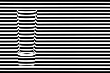 Narrow empty glass against black and white stripes creating illusion of refraction of light