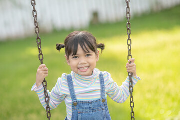 Happy little Asian girl playing swing outdoor in the park