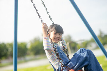 Obraz premium Happy little Asian girl playing swing outdoor in the park