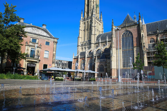Arnhem (Kerkplein), Netherlands - July 9. 2021: View over square with water fountains on medieval gothic church and restaurant cafe against blue summer sky