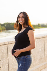 Portrait of hispanic pregnant woman walking in a park at sunset. Pregnancy and motherhood concept.