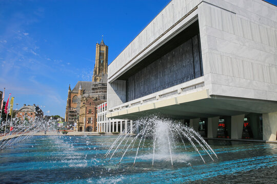 Arnhem (Stadhuis), Netherlands - July 9. 2021: View over water fountain on modern architecture building with medieval church background against blue summer sky