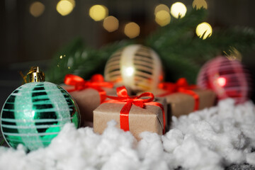 Christmas gifts next to Christmas balls, against the background of flashing lights of a garland in out-of-focus