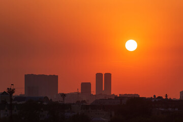 Fototapeta na wymiar Urban skyline during orange sunset. Cityscape and round sun, summer sunset.