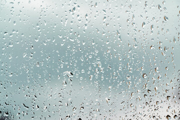 Rain drops on window glasses surface blurred cloudy background, selective focus