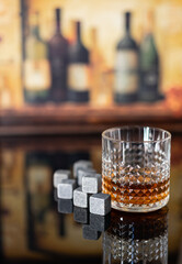 Whiskey with whiskey stones. A glass of whiskey in a crystal glass with whiskey stones in front of a brown background