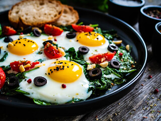 Sunny side up eggs with spinach, cherry tomatoes and black olives on wooden table
