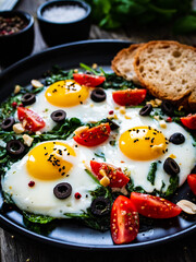 Sunny side up eggs with spinach, cherry tomatoes and black olives on wooden table
