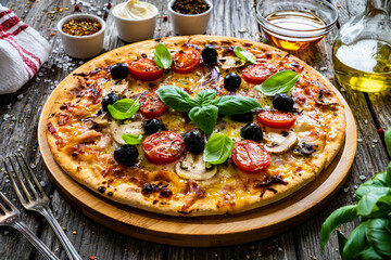 Circle pizza with mozzarella, white mushrooms, salami and tomatoes on wooden table
