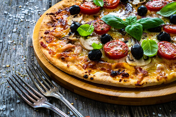 Circle pizza with mozzarella, white mushrooms, salami and tomatoes on wooden table
