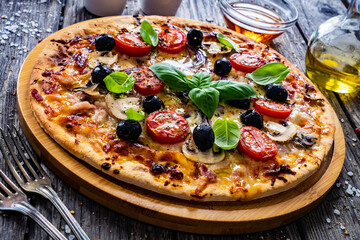 Circle pizza with mozzarella, white mushrooms, salami and tomatoes on wooden table
