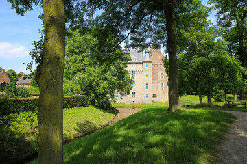 Fototapeta na wymiar View beyond green trees on dutch water castle from 14th century against blue summer sky