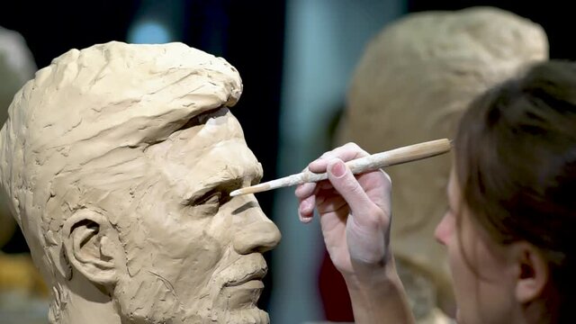 Woman sculptor at work on a sculpture of a human head. The process of restoring the shape of the eyes. Side view. Close up view.