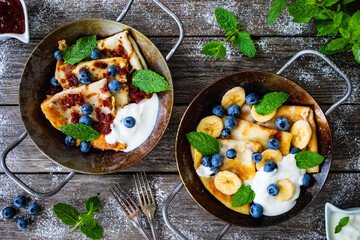 Sweet crepes with strawberries jam and blueberries in pan on wooden table
