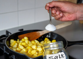 A hand holding full spoon of salt. A man cooking fried potato with too much salt for seasonings ....