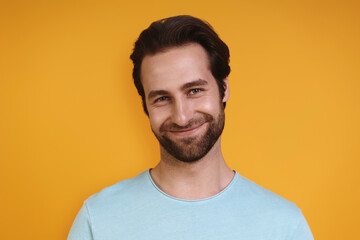 Fototapeta premium Portrait of young man in casual clothing looking at camera and smiling while standing against yellow background