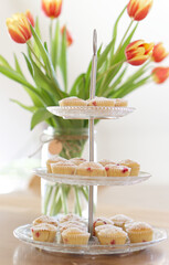 Muffins mit roten Beeren und Puderzucker auf einer Etagere aus Glas mit gelben Tulpen im Hintergrund