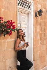 young beautiful woman leaning against typical maltese house holding a vintage camera