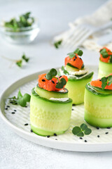 Holiday vegetable appetizers. Cucumbers rolls with soft cheese, pieces of salted salmon, microgreens and black sesame served on a white plate. Selective focus