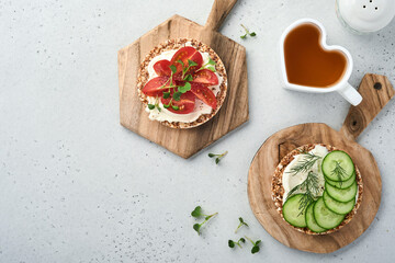 Crispy buckwheat bread cake gluten free with cream cheese, red radish, tomatoes and microgreen for healthy breakfast on grey stone background. View from above. Concept vegan and healthy eating.