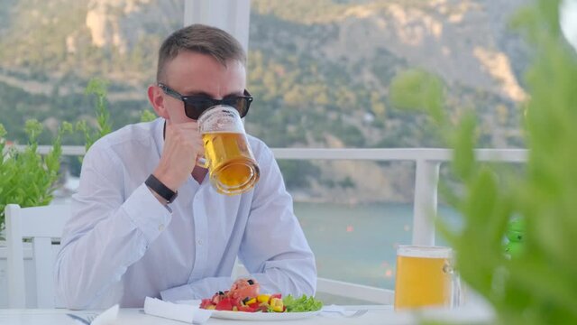 Satisfied man drinks beer at this cafe with vim on the sea
