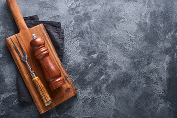 Old meat fork, empty wooden stand, black pepper and black pepper and spice mill on an old gray...
