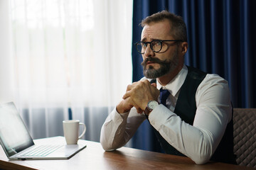 stress bearded businessman distracted and worried with laptop computer on desk over window in office