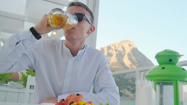 Satisfied man drinks beer at this cafe with vim on the sea
