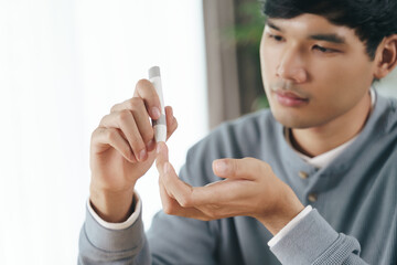 Asian man using lancet on finger for checking blood sugar level by Glucose meter, Healthcare and...