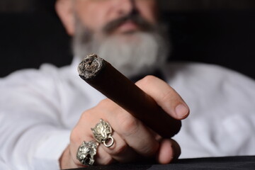 Elegant man wearing white shirt holds a smoking Cuban cigar