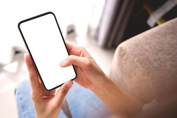Mockup woman hand holding the black smart phone with blank white screen on sofa at home. Business and technology concept