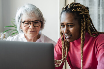 Diverse senior and young woman having video call on laptop computer at home office - Focus on...