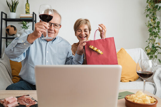 Senior couple celebrating Christmas on video call eating and drinking wine with family - Focus on man face