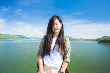 Young happy woman with backpack standing with raised hands and looking to the river. Woman traveling concept