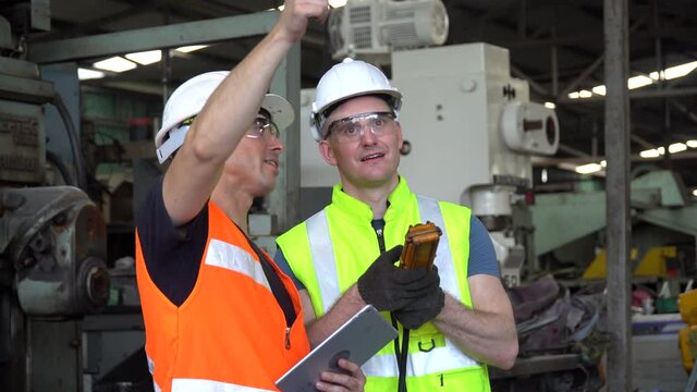 Engineer and technician manager talking together with tablet  controlling by remote control with heavy machine in the industrial plant while the workers are working in Industrial factory .