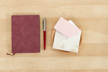 Notebook, pen and pink blank paper card with rustic envelope, recycled paper, on wooden desk.