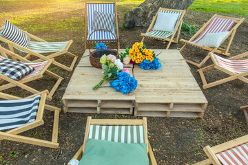 Beautiful artificial bouquets of various colors placed on wooden table among deck chairs in garden....